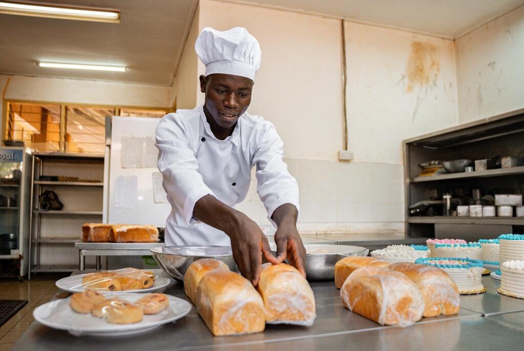 Mwokaji katika jikoni la kitaalamu hupanga mikate iliyookwa hivi karibuni kwenye kaunta ya chuma.