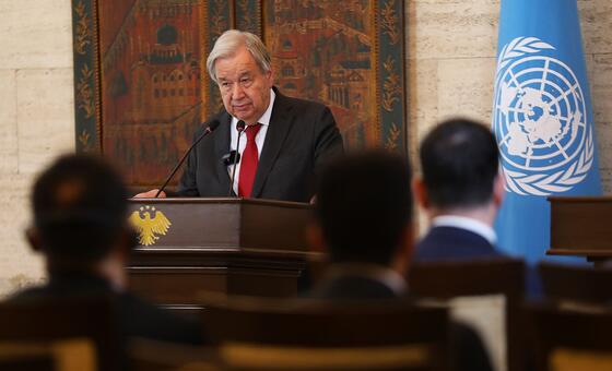 UN Secretary-General António Guterres speaks at a podium during a meeting, with the UN flag visible in the background.
