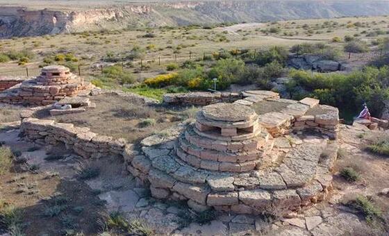 Древние каменные руины объекта Всемирного наследия UNESCO в Казахстане, представляющие собой круглые башни и укрепленные стены на обширной засушливой степной местности.