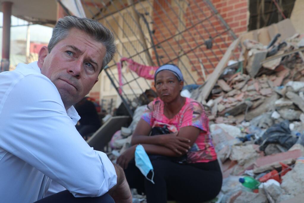 Un trabajador humanitario y una mujer se sientan entre los escombros de un edificio derrumbado en Venezuela.