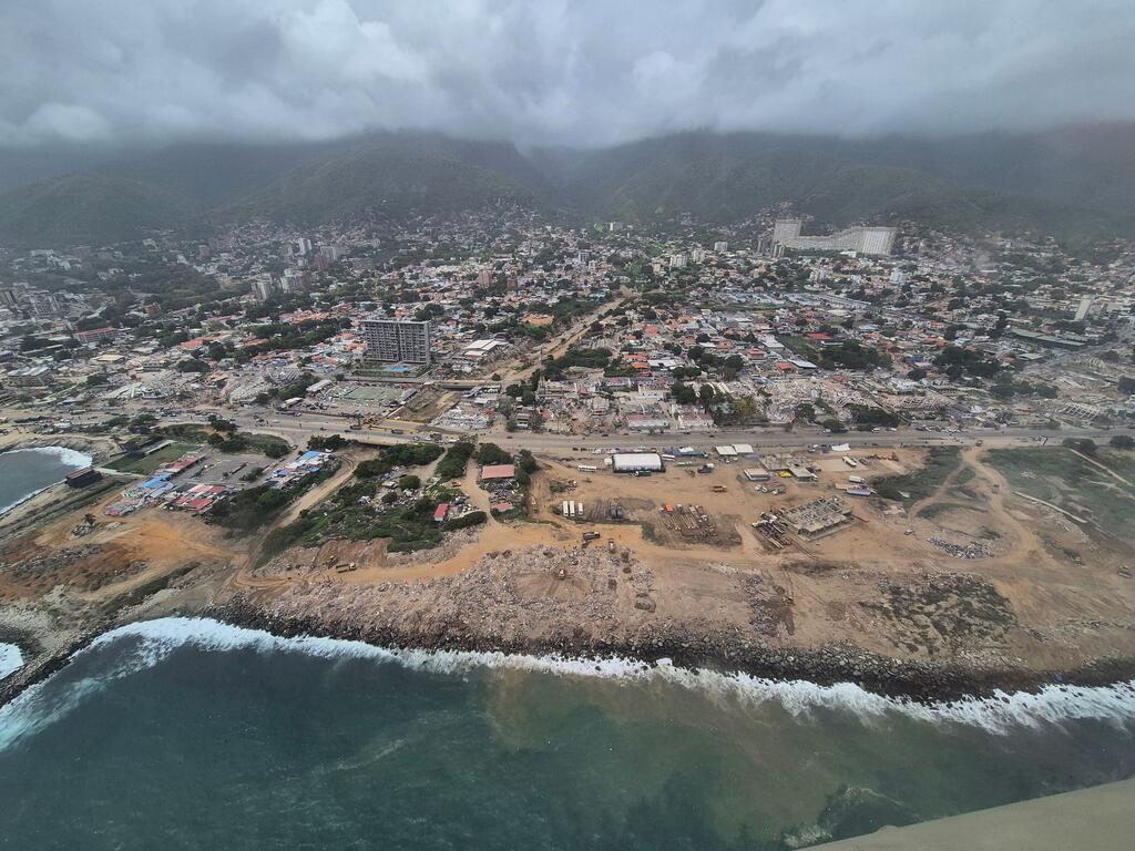 Vista aérea de una ciudad costera de Venezuela, con montañas al fondo y una obra en construcción cerca de la playa.