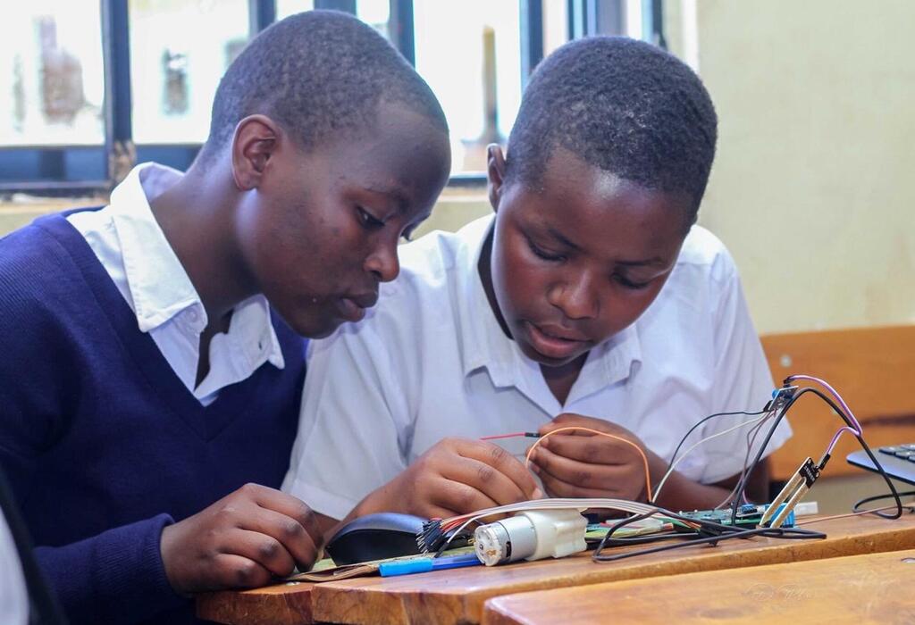 Wavulana wawili wadogo darasani wanafanya kazi pamoja katika mradi mdogo wa kielektroniki unaohusisha waya na vipengele kwenye dawati la mbao.