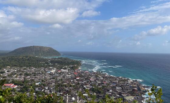 Une ville côtière des médinas des sultanats historiques des Comores, avec une mosquée visible au premier plan et une colline surplombant l'océan Indien.