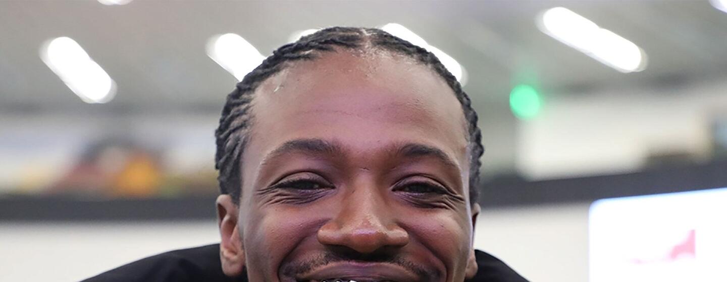 Primer plano de un hombre afroamericano sonriente con el pelo trenzado, que lleva una chaqueta negra y una parrilla dental plateada.