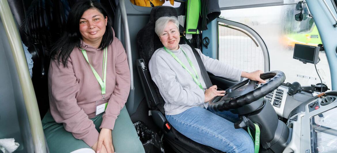 Three women are inside a bus, one driving while two others look on. The scene relates to UN Women's work in Ukraine on recovery and women's empowerment.