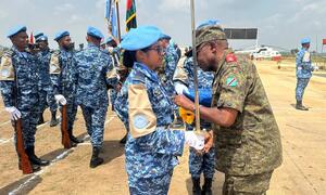 Mlinda amani UN wa kike kutoka Bangladesh aliyevaa sare ya bluu akipokea medali kutoka kwa afisa wa kiume aliyevaa mavazi ya kujificha kwenye uwanja wa ndege.