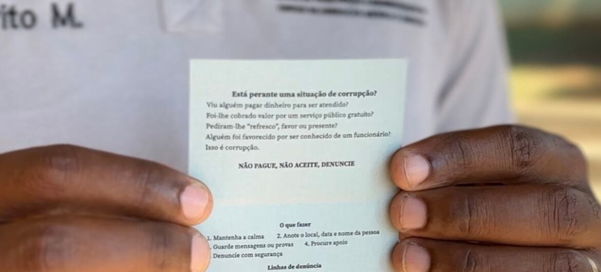 Uma pessoa segura um cartão com informações sobre como denunciar a corrupção em Moçambique.