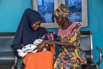 Une femme âgée soutient une jeune femme qui allaite son bébé lors d'une consultation postnatale dans un centre de santé primaire à Ibadan, au Nigéria.