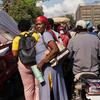 Une femme portant un foulard rouge se tient dans une rue haïtienne bondée, au milieu de motos et de camions.