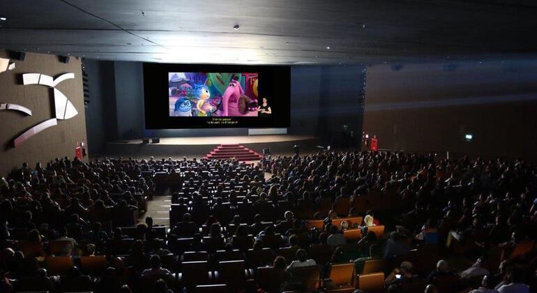 Uma visão ampla de uma sessão de cinema lotada em uma sala moderna, com um filme de animação exibido na tela grande à frente.
