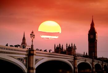 Big Ben and the Houses of Parliament in London silhouetted against a large, glowing orange sun during a heat wave.