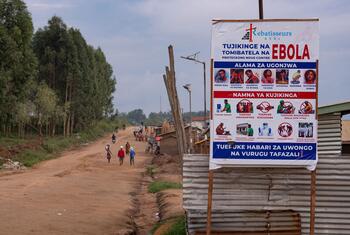 Un cartel de prevención del ébola se encuentra junto a un camino de tierra en la provincia de Ituri, República Democrática del Congo, mientras la gente camina por el sendero.