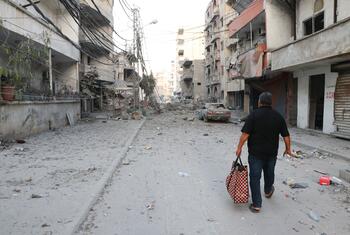 Un homme portant un sac marche dans une rue de Tyr, au Liban, jonchée de gravats et de débris suite à une frappe aérienne israélienne.