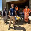 ورلڈ فوڈ پروگرام (WFP) کا ایک مرد امدادی کارکن خوراک کی تقسیم کے آپریشن کے دوران مقامی عملے کے ساتھ گودام کے سامنے کھڑا ہے۔