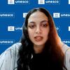 تتحدث هايدي ميرزا، أخصائية البرامج الوطنية في قطاع الاتصالات والمعلومات الحربية بمكتب UNESCO في الخرطوم، السودان، أمام خلفية زرقاء عليها شعارات UNESCO المتكررة.