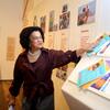 Maria Angela de Jesus está em frente a uma vitrine, apontando para uma pilha de livros infantis coloridos.