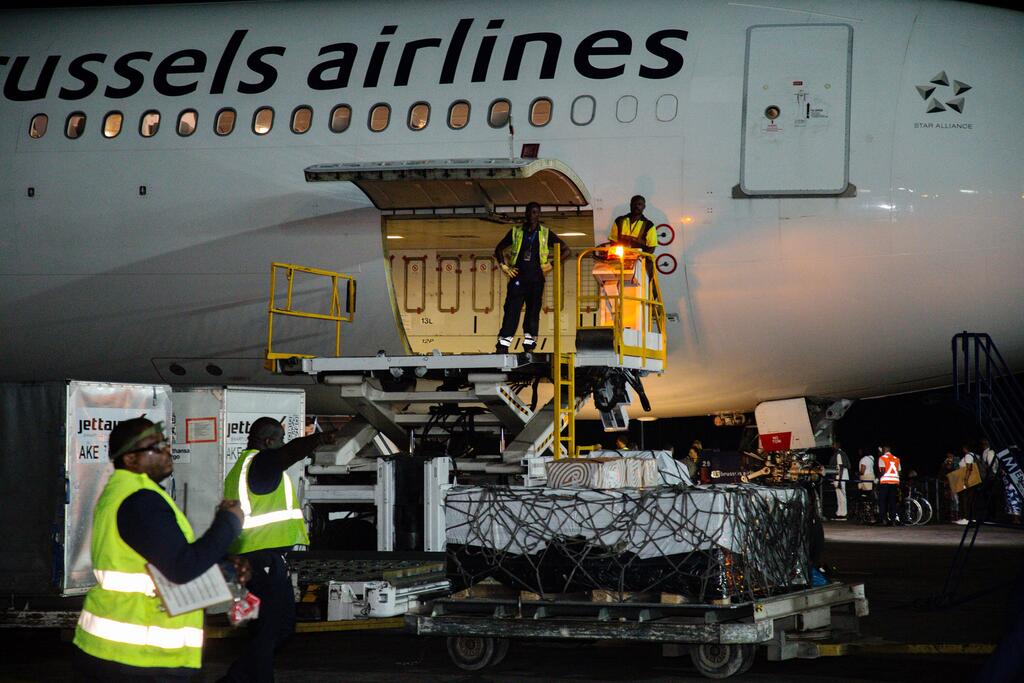 Wafanyakazi wa uwanja wa ndege wakiwa wamevaa fulana za usalama wakipakia kreti za chanjo za Ebola kwenye ndege ya shirika la ndege la Brussels usiku.