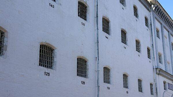 Gros plan sur l'extérieur d'un bâtiment de prison blanc avec des fenêtres à barreaux et des numéros de cellules comme 125 et 145.