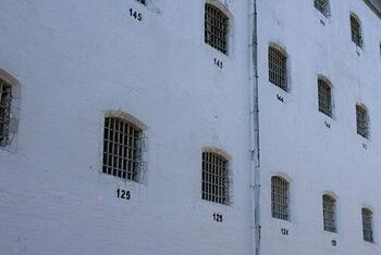 A close-up view of a white prison building exterior with barred windows and cell numbers like 125 and 145.
