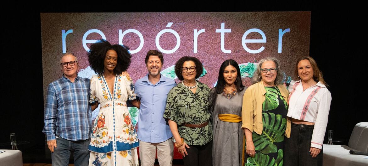 Maria Angela de Jesus e outras seis pessoas posam para uma foto de grupo em frente a um painel de fundo da TV Cultura Reporter Eco.