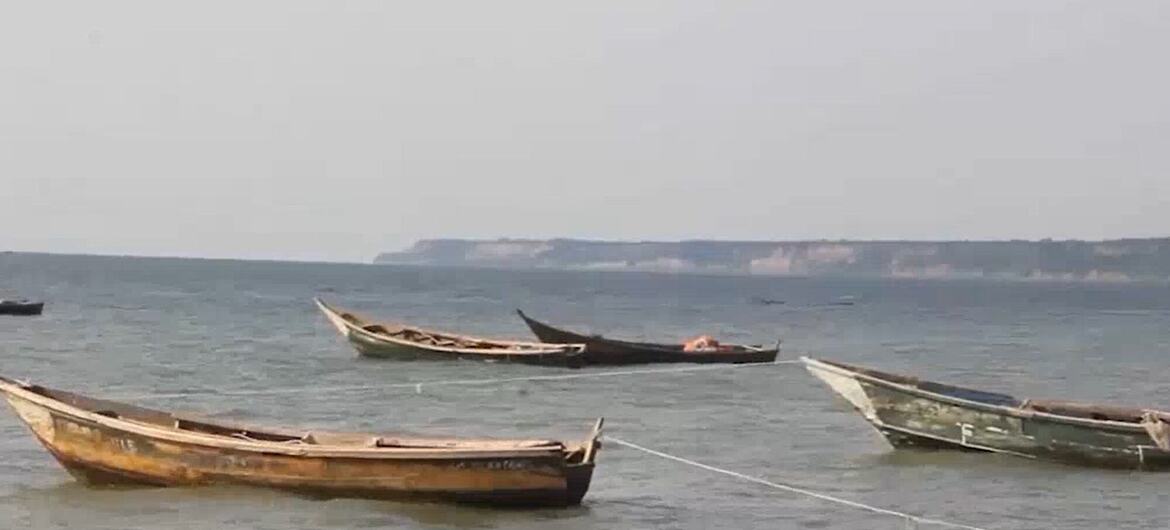 Traditional wooden fishing boats anchored on the calm waters of Lake Albert in Uganda under a hazy sky.