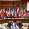 Diplomáticos sentados en una mesa curva en una sala de conferencias de las Naciones Unidas , con las banderas nacionales de los estados miembros dispuestas detrás de ellos y una pantalla que muestra a un orador remoto.