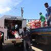 Funcionários do WFP e trabalhadores locais descarregam sacos de alimentos vermelhos e brancos de um veículo anfíbio SHERP do WFP para um caminhão plataforma azul na cidade de Xai-Xai, Moçambique.