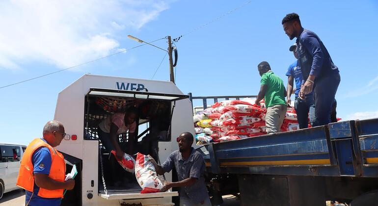 Funcionários do WFP e trabalhadores locais descarregam sacos de alimentos vermelhos e brancos de um veículo anfíbio SHERP do WFP para um caminhão plataforma azul na cidade de Xai-Xai, Moçambique.
