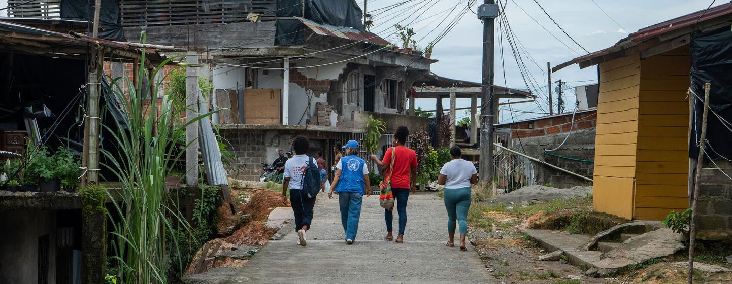 Cuatro personas caminan por una calle de cemento, pasando junto a casas con techos derrumbados y paredes al descubierto, en un barrio de Chocó, Colombia, dañado por el terremoto.