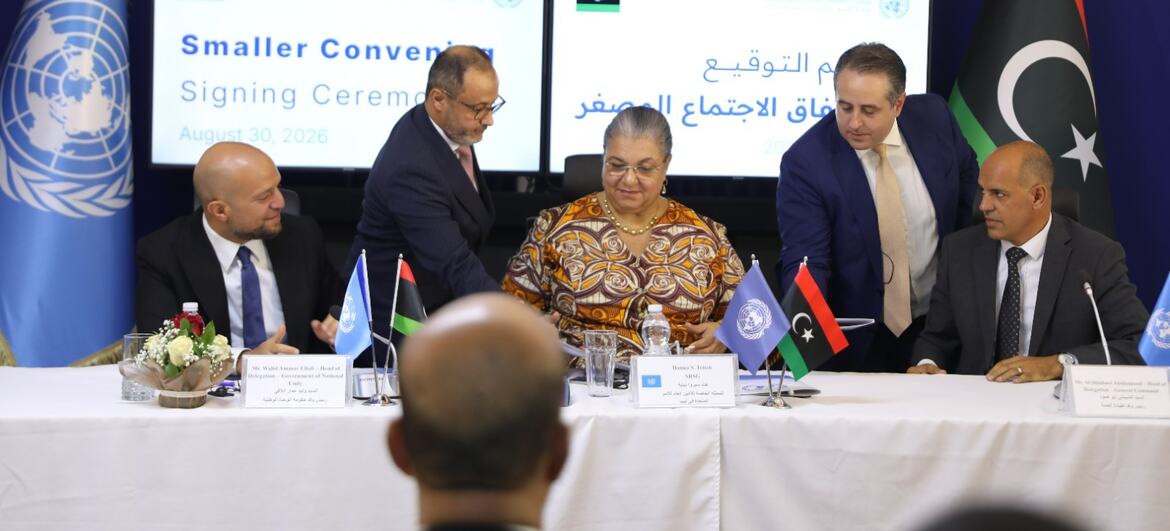 الممثل الخاص لبعثة الأمم المتحدة للدعم في ليبيا (في الوسط) يوقع اتفاقاً بشأن الإطار الانتخابي في ليبيا خلال حفل التوقيع، مع ظهور علمي الأمم المتحدة وليبيا في الخلفية.