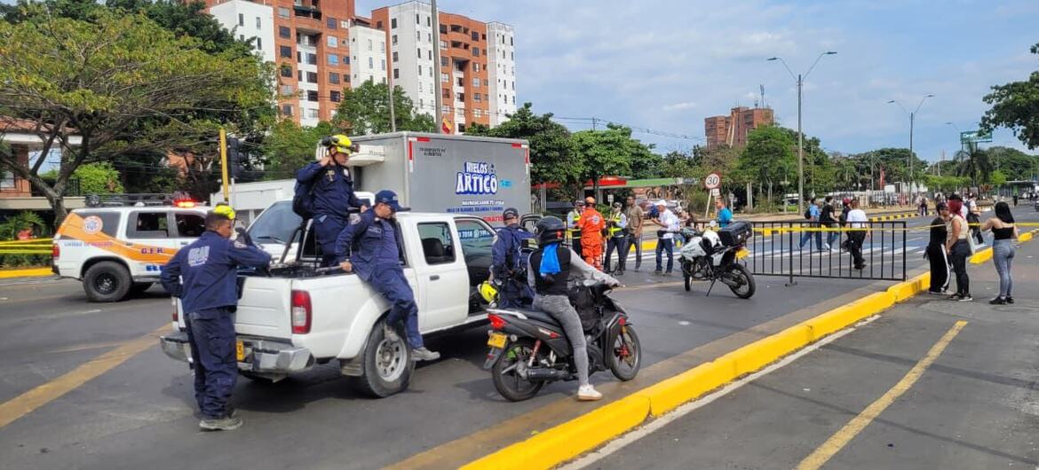 Police officers in blue uniforms and yellow helmets stand guard at a street checkpoint next to a white pickup truck.