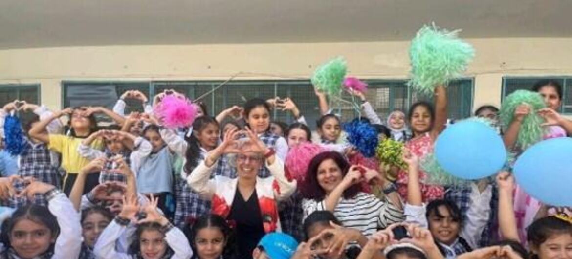 مجموعة من طالبات المدارس يرتدين زيًا موحدًا منقوشًا ومعلمة يقفن في الهواء الطلق ويشكلن أشكال قلوب بأيديهن بينما يحملن بالونات ملونة وكرات صوفية.