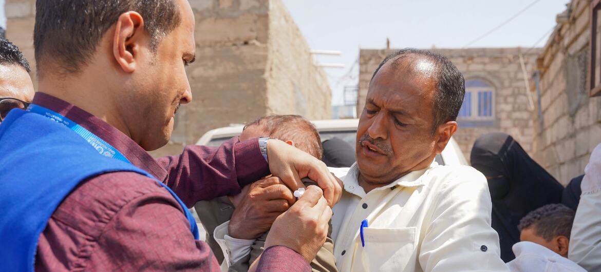 يقوم أحد العاملين في مجال الرعاية الصحية التابعين للمنظمة الدولية للهجرة بإعطاء لقاح الحصبة لطفل رضيع يحمله والده خلال حملة تطعيم طارئة في محافظة مأرب باليمن.