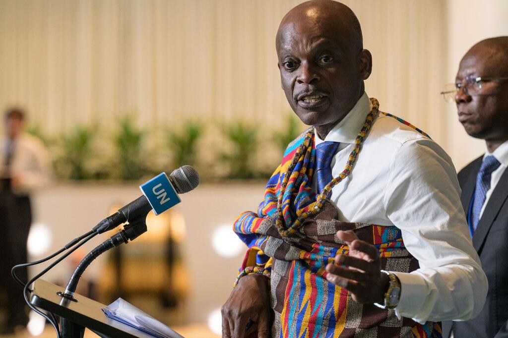 Un Togolais vêtu d'un tissu traditionnel tissé et d'une chemise blanche prend la parole au micro, portant le logo de l'ONU, lors d'une réunion officielle.