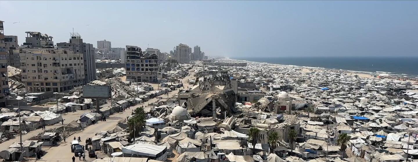 Vue aérienne d'un immense campement de tentes et de bâtiments endommagés le long du littoral de la bande de Gaza, près de la mer Méditerranée.