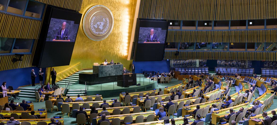 Wide-angle view of the United Nations General Assembly Hall during the closing of the 80th and opening of the 81st session, with delegates seated in curved rows facing the rostrum beneath the UN emblem.