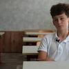 صورة التقطتها UNICEF لفتى مراهق يرتدي قميص بولو أبيض اللون ويحمل ميكروفوناً لاسلكياً يجلس على مكتب في فصل دراسي فارغ في أوكرانيا.