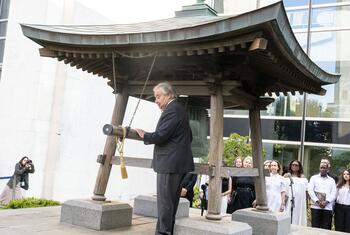 UN Secretary-General António Guterres stands beside a large Japanese Peace Bell at the United Nations headquarters in New York during a ceremonial event.