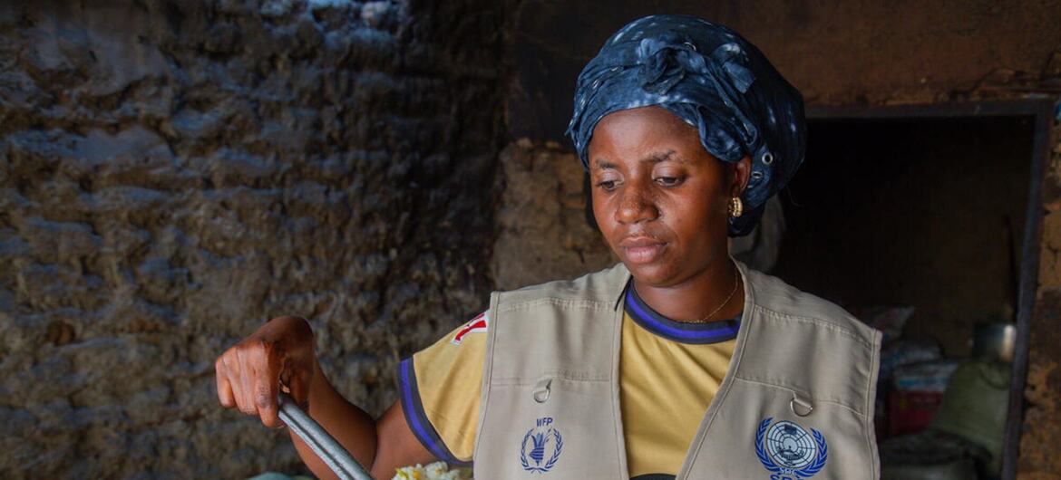A female WFP field worker in the Democratic Republic of Congo wearing an IFP/SDC vest serves a spoonful of cooked rice during hot meal preparation in an Ebola response effort.