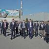 Делегация UNDP идет по промышленной площадке перед заводским зданием, на котором изображено большое панно, показывающее руки, держащие земной шар.