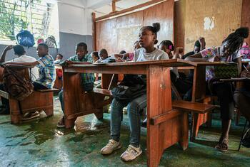 Un groupe de jeunes étudiants haïtiens sont assis à des tables en bois dans une salle de classe, prenant des notes et étudiant.