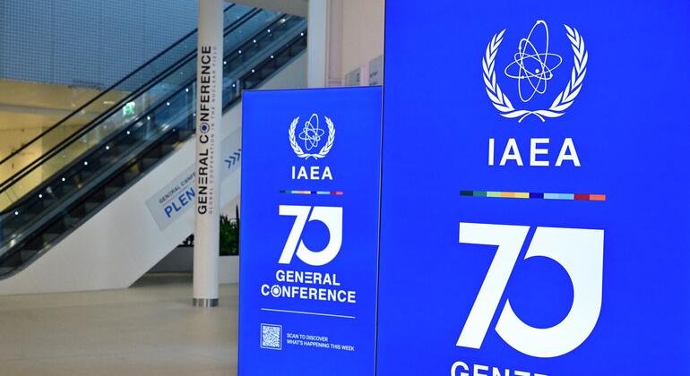 تنتصب لافتتان زرقاوان طويلتان تحملان شعار الوكالة الدولية للطاقة الذرية (IAEA)، ورقم "70" كبير، وعبارة "المؤتمر العام"، وذلك في قاعة مؤتمرات مشرقة تضم سلالم متحركة وعموداً يحمل علامة المؤتمر.