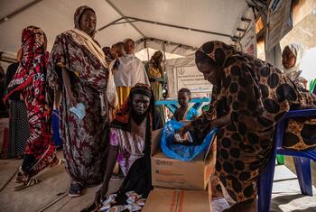 South Sudanese women and children at a nutrition center in Wedweil refugee settlement, Northern Bahr el Ghazal, as a woman distributes nutritional supplements from a USAID-marked box.