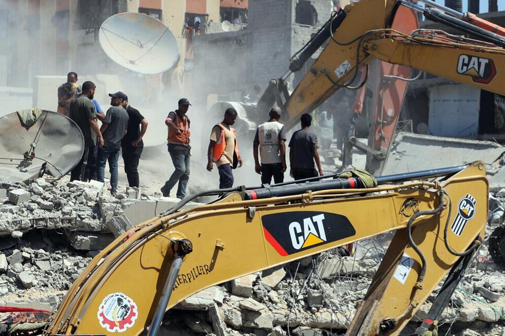 À Gaza, des hommes se tiennent près d'une excavatrice Caterpillar jaune au milieu des décombres, de la poussière et des antennes paraboliques endommagées provenant des bâtiments détruits.
