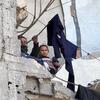 À Gaza, deux enfants regardent au loin depuis un mur de béton endommagé, tandis que des vêtements sèchent sur une corde tendue au-dessus des décombres.