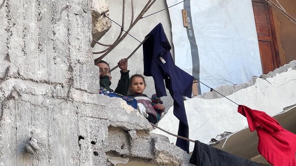 À Gaza, deux enfants regardent au loin depuis un mur de béton endommagé, tandis que des vêtements sèchent sur une corde tendue au-dessus des décombres.