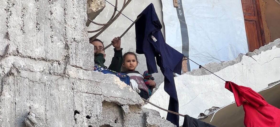 À Gaza, deux enfants regardent au loin depuis un mur de béton endommagé, tandis que des vêtements sèchent sur une corde tendue au-dessus des décombres.