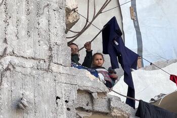 À Gaza, deux enfants regardent au loin depuis un mur de béton endommagé, tandis que des vêtements sèchent sur une corde tendue au-dessus des décombres.