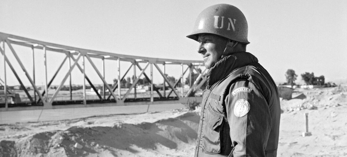 Austrian Army Captain Josep Muller in a United Nations helmet and uniform stands at an observation post near the Suez Canal, with a steel bridge in the background.