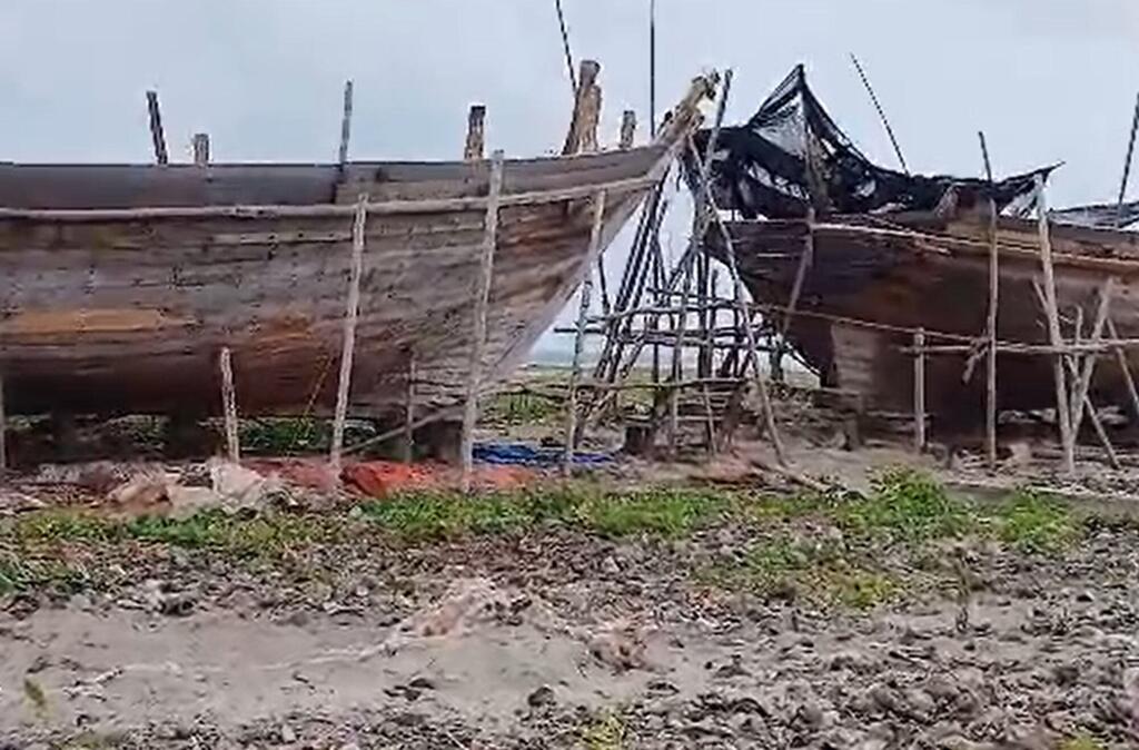 Des barques de pêche en bois patinées par le temps reposent sur une rive sablonneuse, soutenues par des poteaux en bois, des filets sombres drapés sur l'une d'elles sous un ciel couvert.
